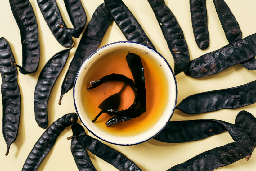 A bowl of boiled honeylocust black dried pods on yellow background. Honeylocust or Gleditsia triacanthos dried pods, containing natural saponins, are boiled to wash the hair, believed to promote growth and smoothness, as well as address dandruff.