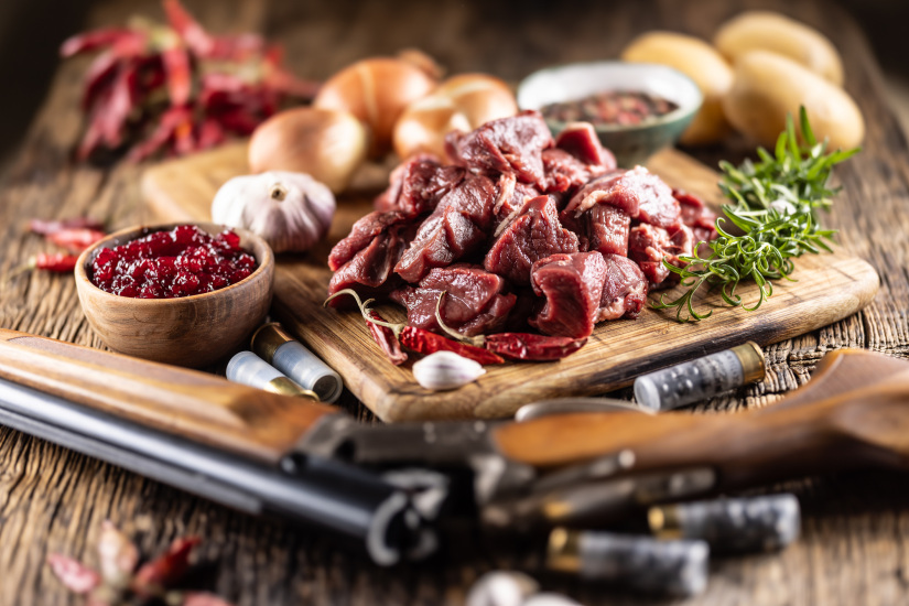 Sliced ââfresh deer or elk meat with rosemary spices and cranberry dip. As a decoration, a hunting gun with bullets.