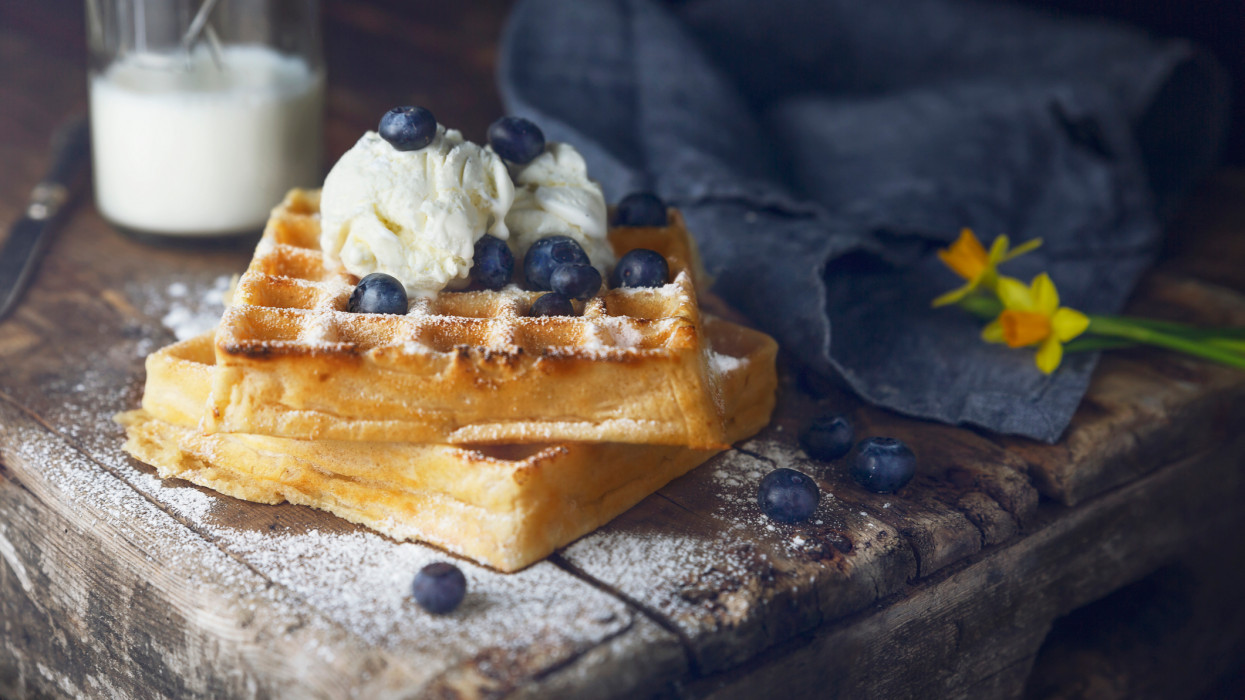 A close-up of a belgian waffle with ice cream, blueberries, milk and powdered sugar.