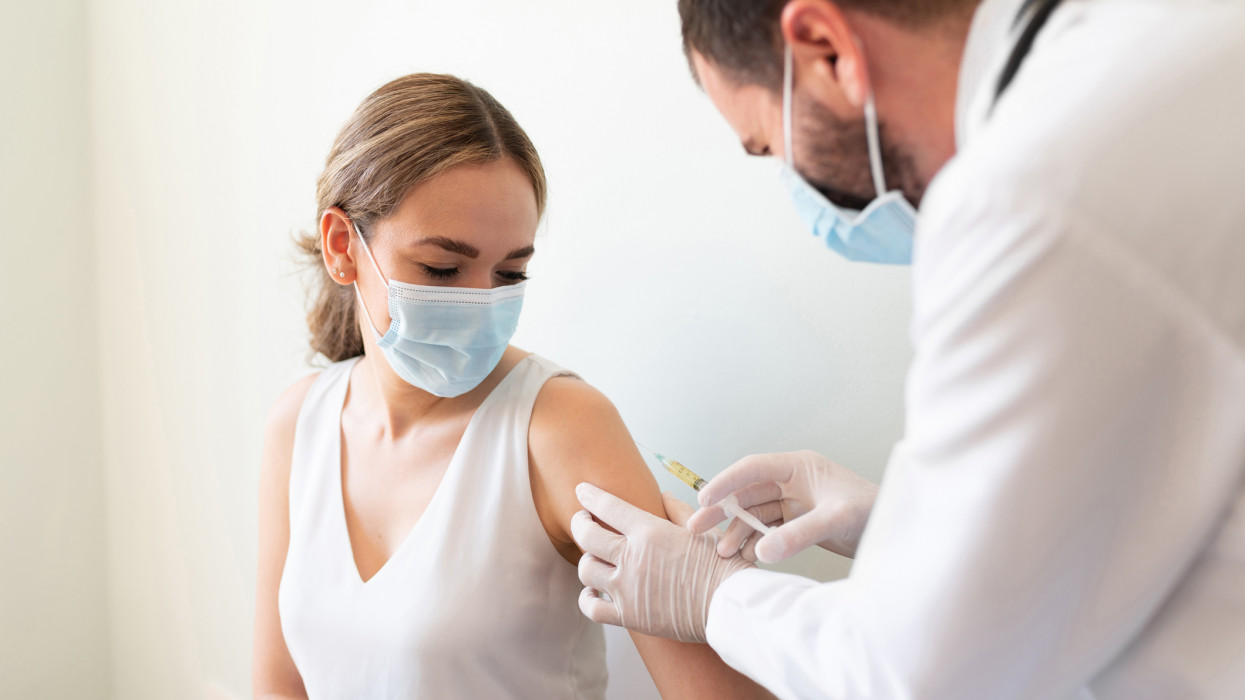 Closeup of a nervous woman and her doctor wearing face masks and getting a vaccine shot in a doctors office