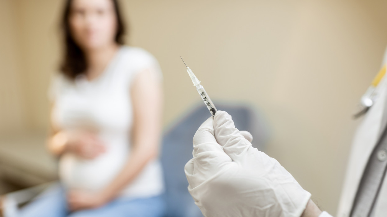 Doctor holding vaccine or some medication in the syringe, preparing for injection for a pregnant woman during a medical procedure in the clinic, close-up view