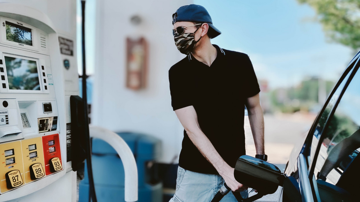 Mid adult man pumps gas wearing protective face mask during COVID-19 pandemic