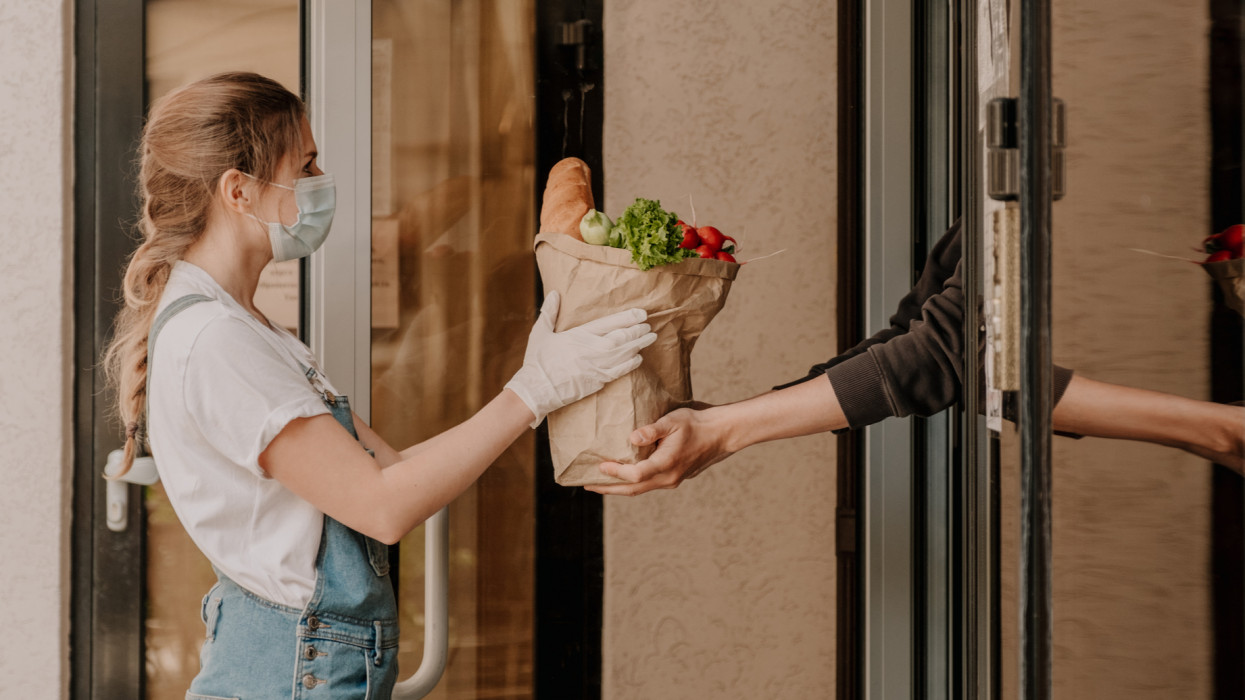 Delivering food ordered online while in home isolation during quarantine. Stay home we deliver. A young girl in a protective mask and gloves delivers food around the city.