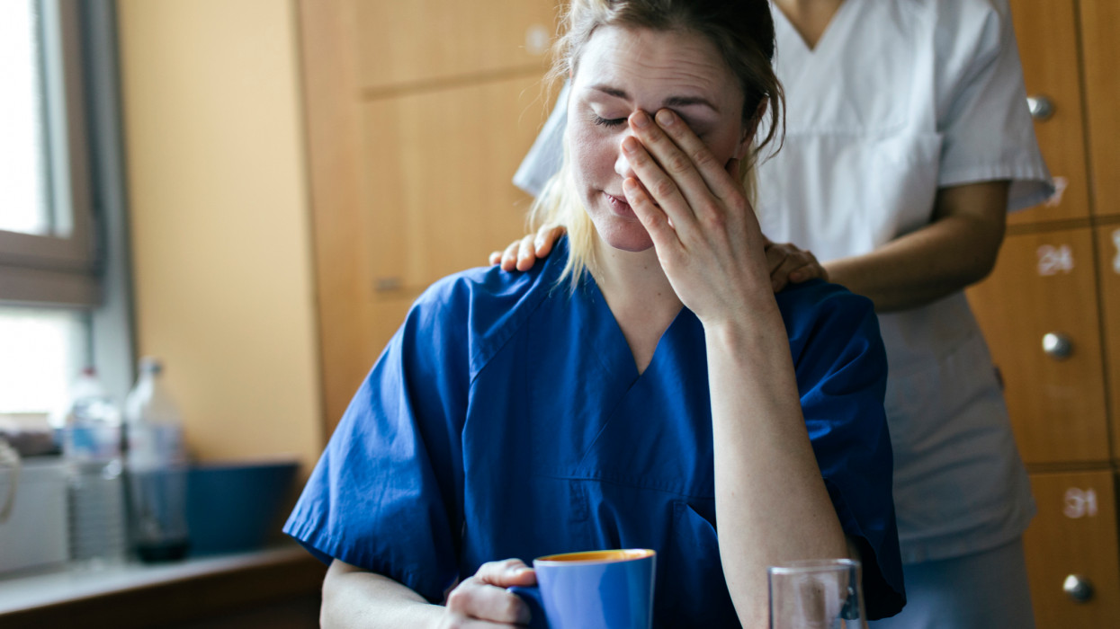 Nurse consoling a young female doctor sitting in a break room
