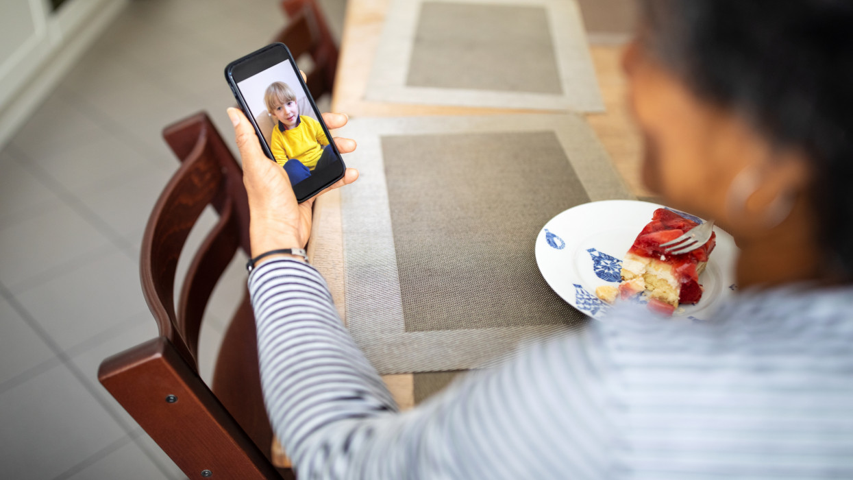 Woman using mobile phone and having video call with her grandson during covid-19 pandemic. Mature woman having video call on mobile phone while having breakfast at home.