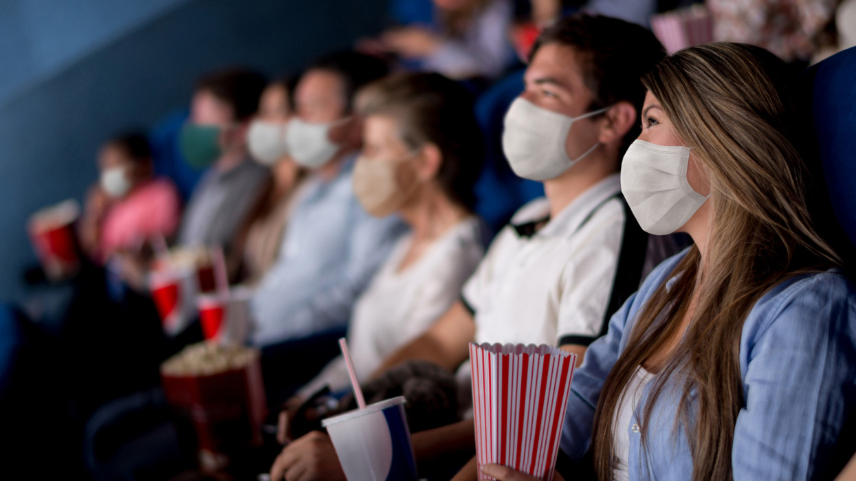 Group of people at the cinema wearing facemasks while watching a movie - reopening of businesses