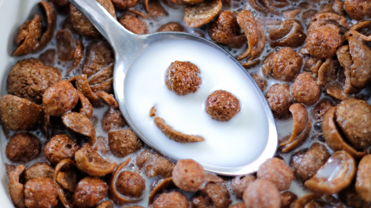 Smiling chocolate cereals in the spoon with cereals in a bowl on background