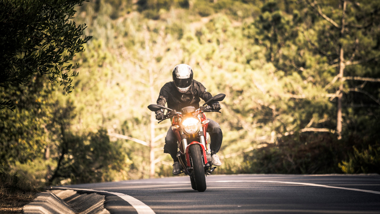 A solo motorcyclist takes to the winding country lanes of Sintras dense forest. The canopy of trees creates shadow for the rider, so the headlights are necessary during a day trip.