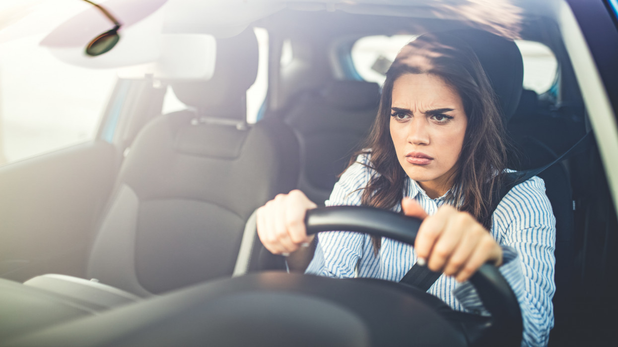 Frustrated woman stuck in traffic. Young woman gets annoyed while driving the car in traffic jam. Portrait displeased angry pissed off aggressive woman driving car.