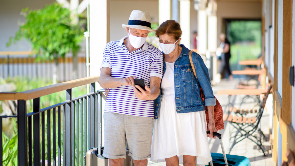 Senior couple with face masks and luggage outside apartment on holiday, back to normal concept.