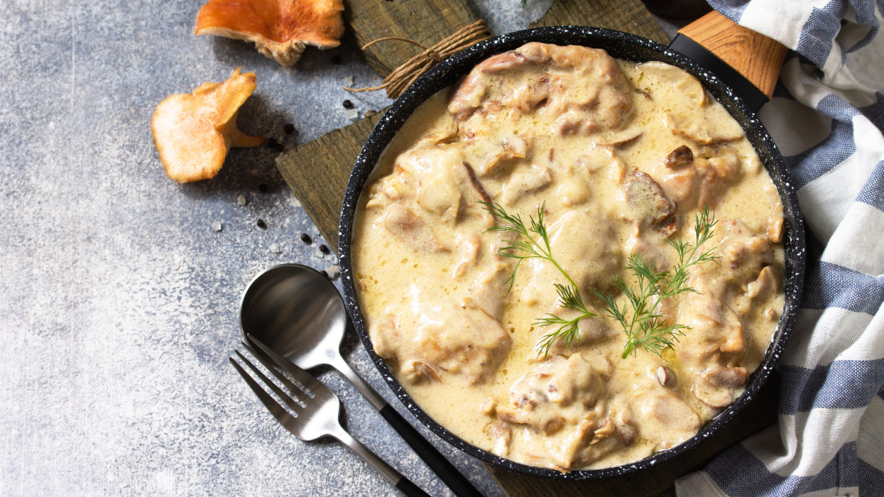 Fricasse - French Cuisine. Chicken stewed in a creamy sauce with mushrooms in a pan on a light stone background. Copy space.