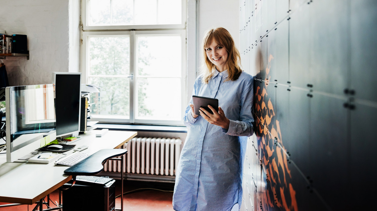 A portrait of a startup business owner standing in her office holding a digital tablet.