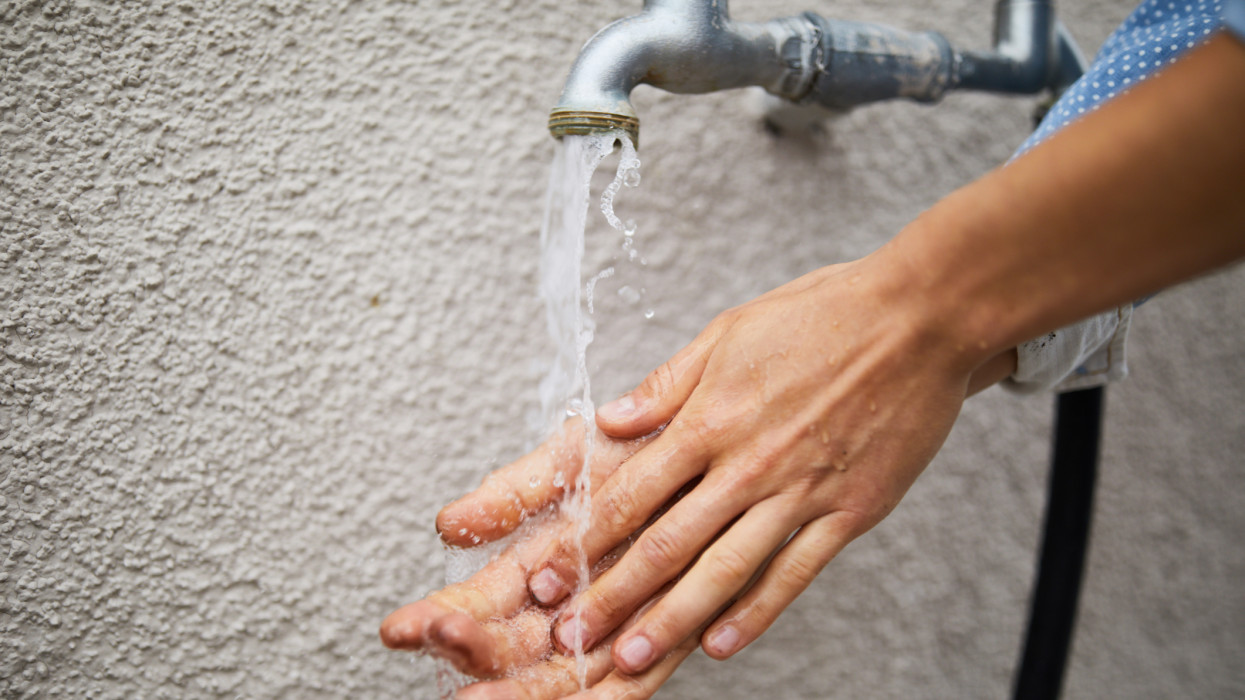 Cropped image of woman washing hands under faucet against wall