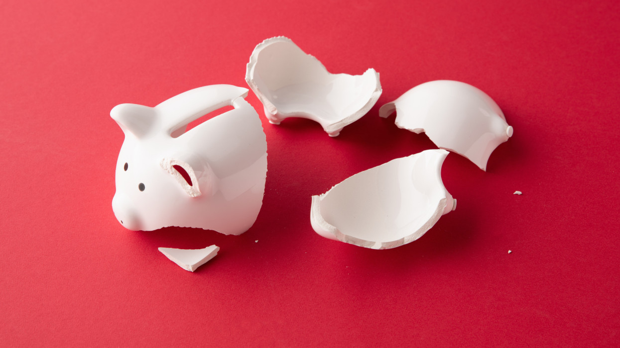 Broken whiter ceramic piggy bank in pieces on red surface
