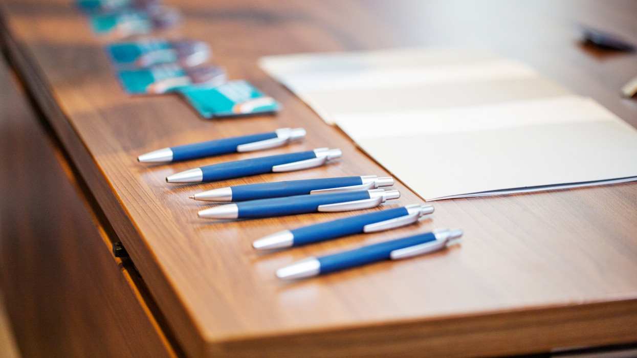 Set of pens and notepads with ID cards on office table. Writing instruments organized in order. Concept is of global communications meeting.