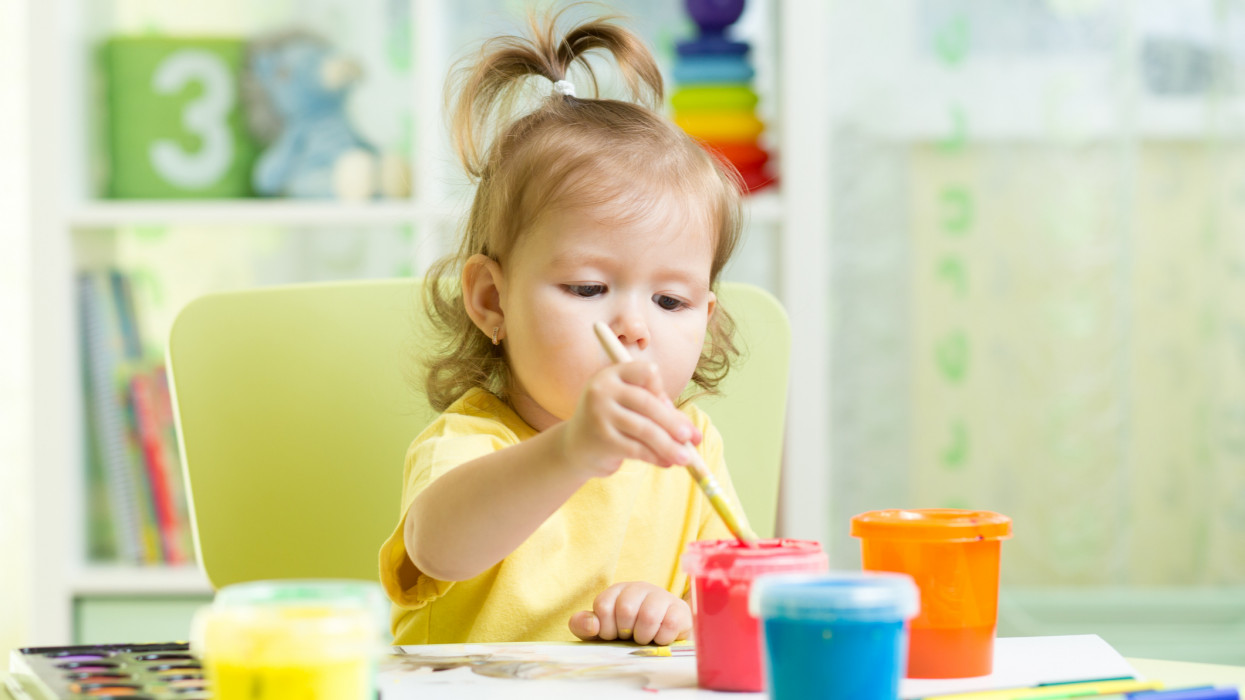 Little girl painting with colorful paints at table