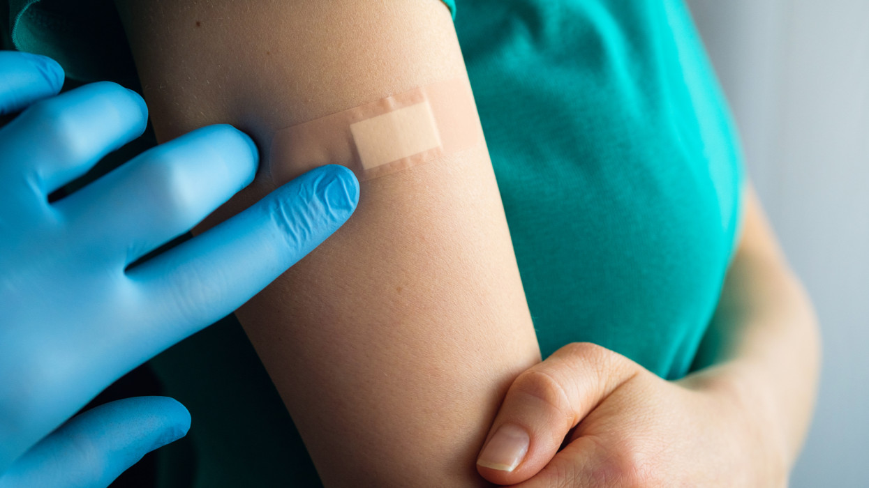 A doctor or health care professional applies a patch or adhesive bandage to a girl or young woman after vaccination or injection of medication. The concept of medicine and health care, vaccination and treatment of diseases. First aid.