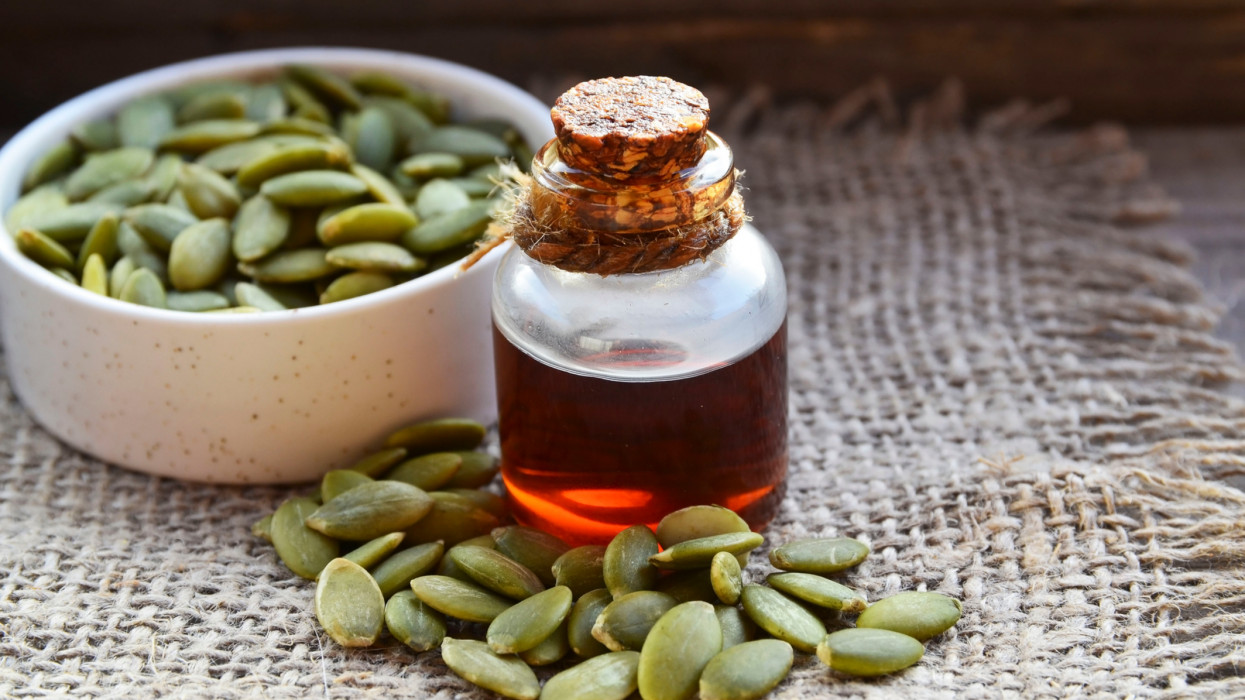 Pumpkin seed oil in a glass jar and fresh raw seeds on old wooden table.Healthy eating,diet or vegan food concept.Selective focus.