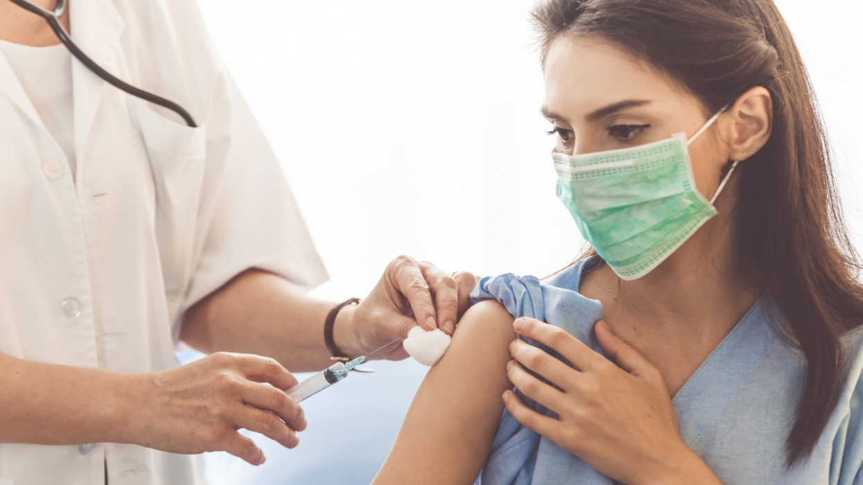 Doctor giving patient vaccine, flu or influenza shot or taking blood test with needle. Nurse with injection or syringe. Cropped image of handsome mature doctor in protective gloves making woman an injection