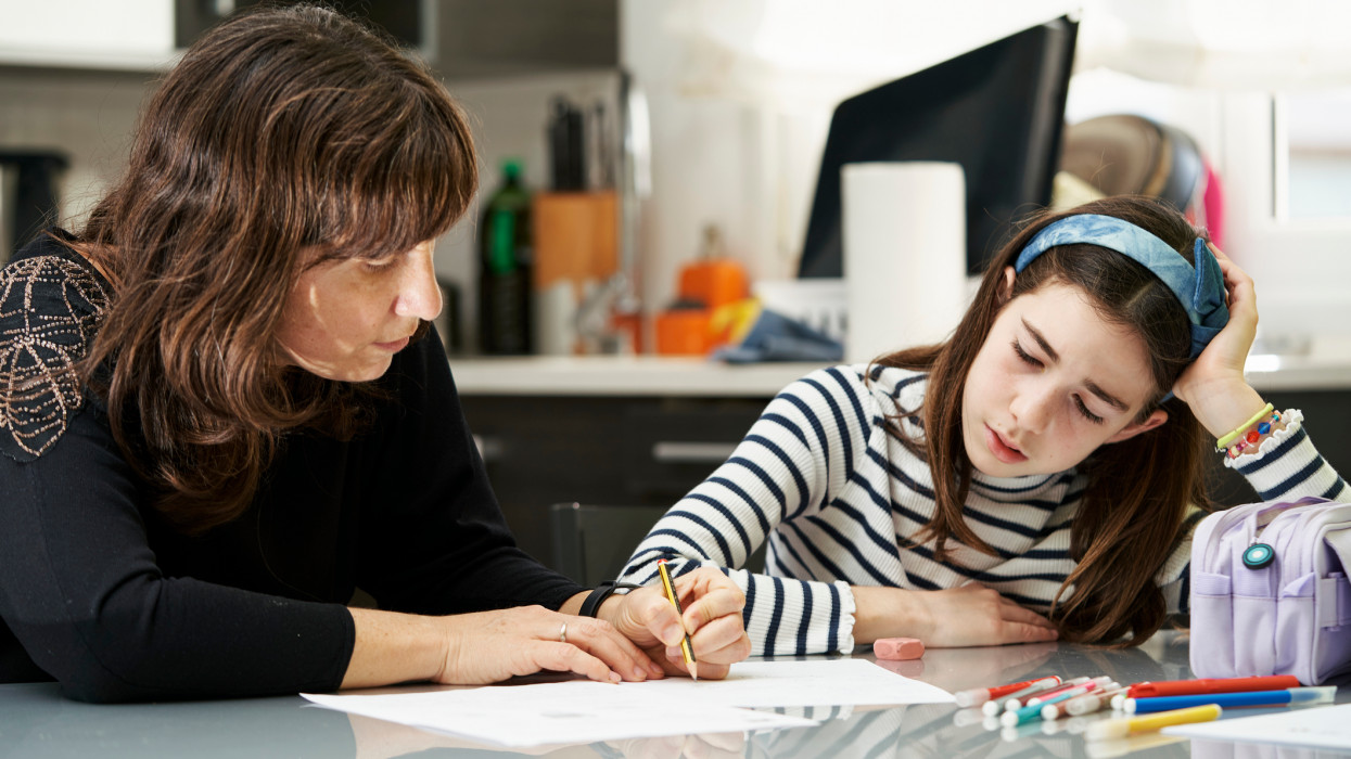 Mother helping her daughter with the school homework at home. Education concept.