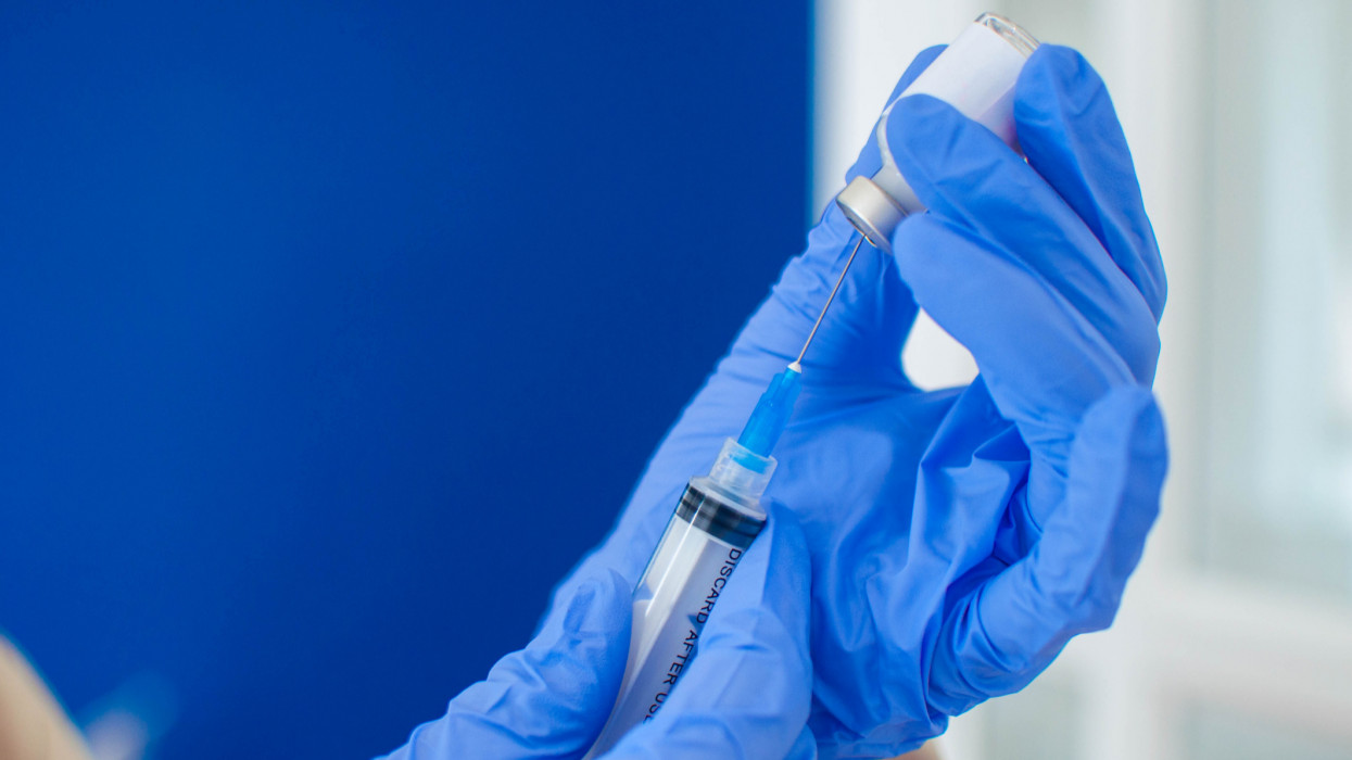 A close-up view of a young doctor in blue protective glove is holding a medical syringe and vial