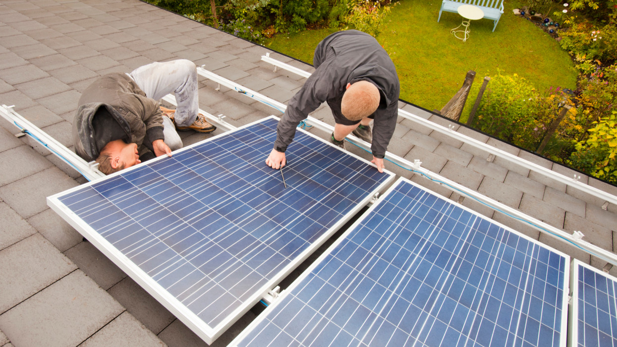 Technicians fitting solar photo voltaic panels to a house roof in Ambleside, Cumbria, UK.