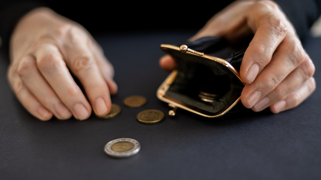 The hands of an elderly woman take out the last coins from the savings in a black wallet, the concept of poverty