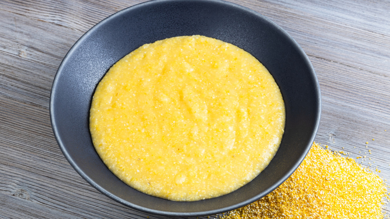 cooked maize porridge in gray bowl and handful of cornmeal on gray wooden table