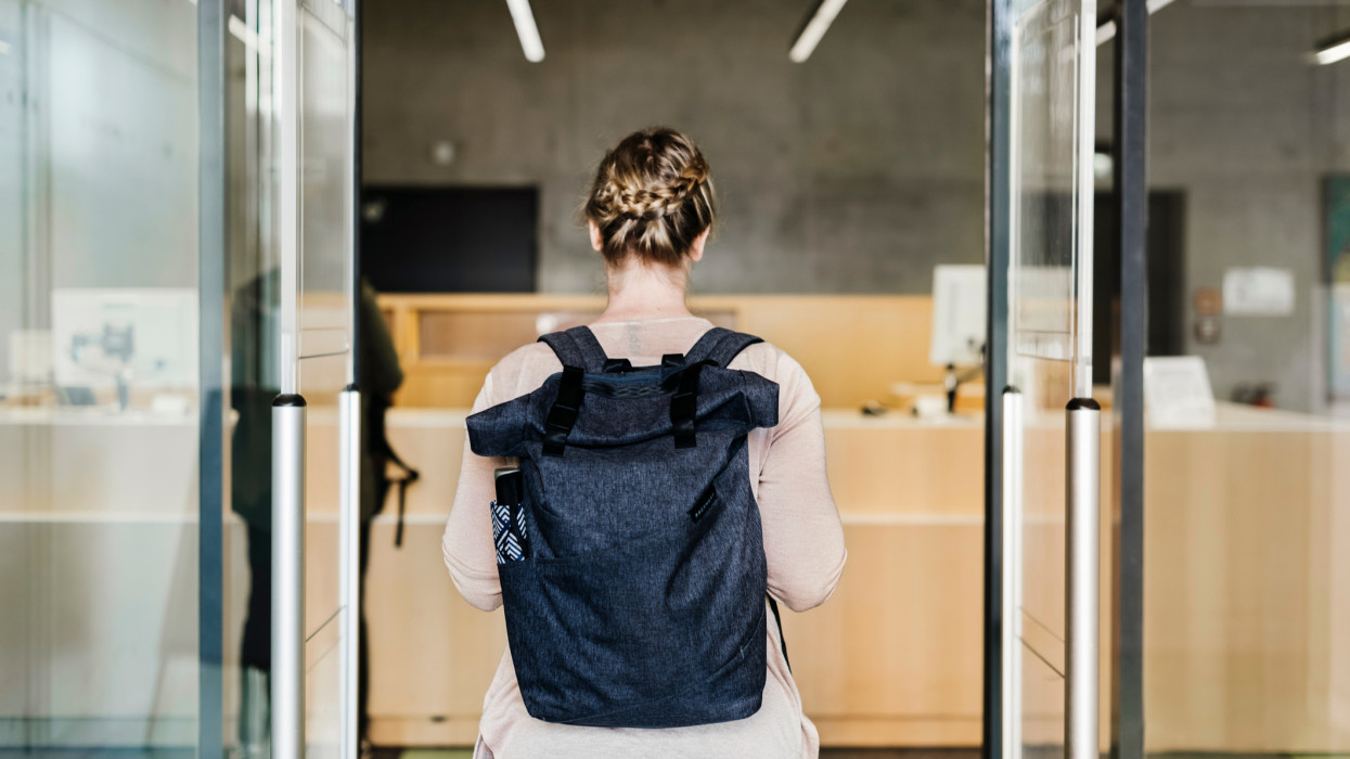 A woman wearing a backpack walking through the entrance to a public library,