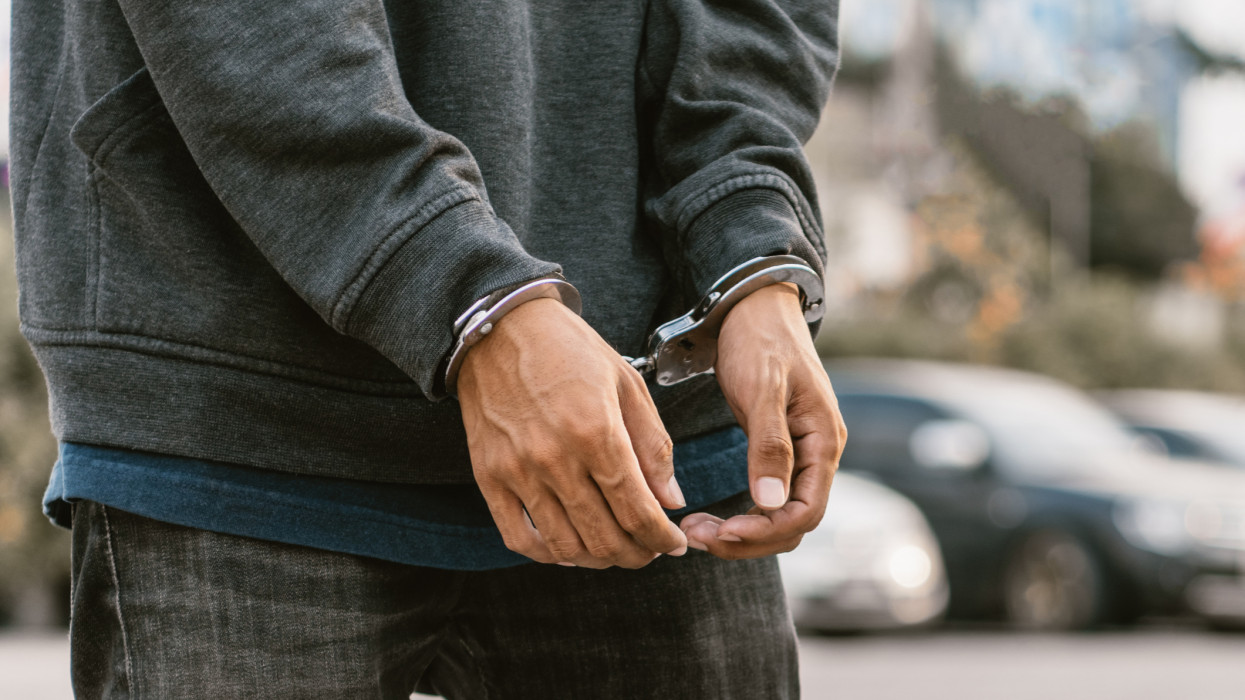 Under arrest, a mans hands with clenched fists are handcuffed behind him. Black background with copy space.