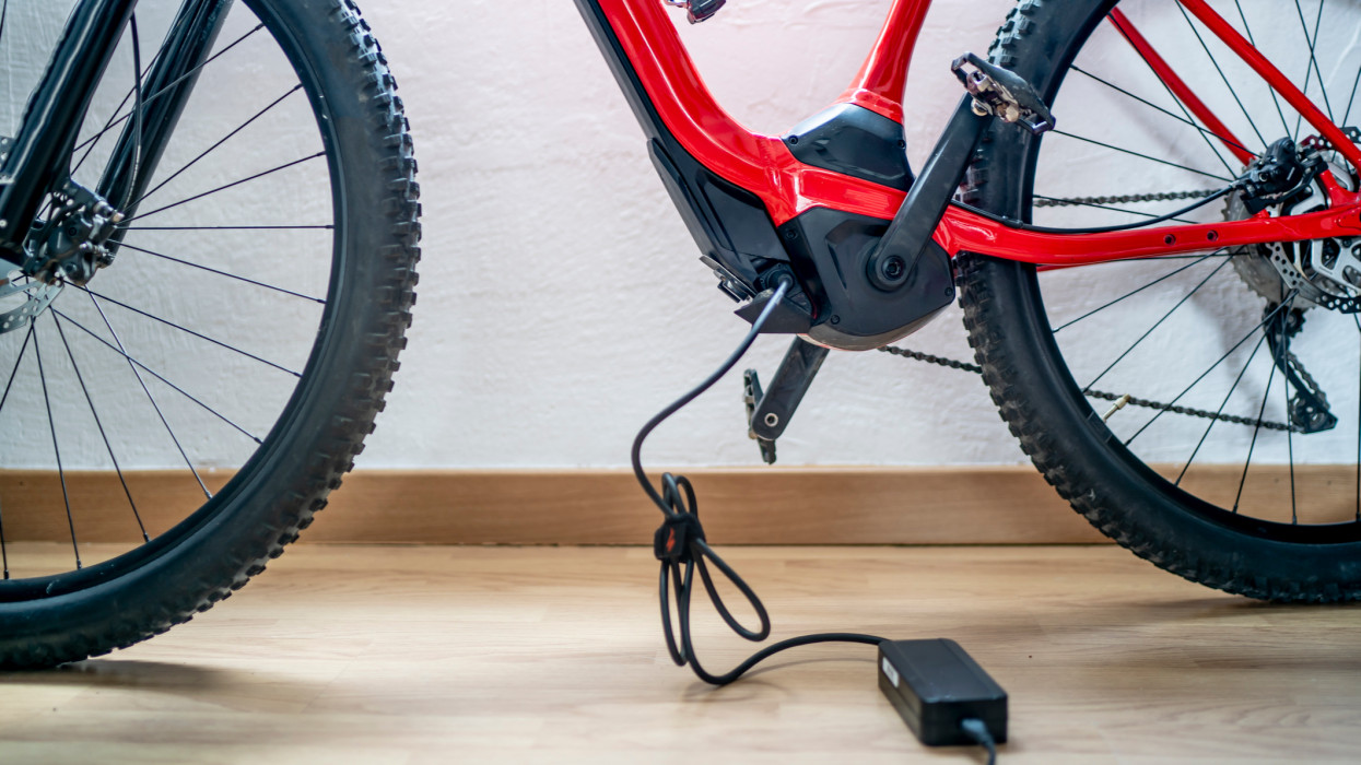 Electric mountain bike charging battery next to home window.