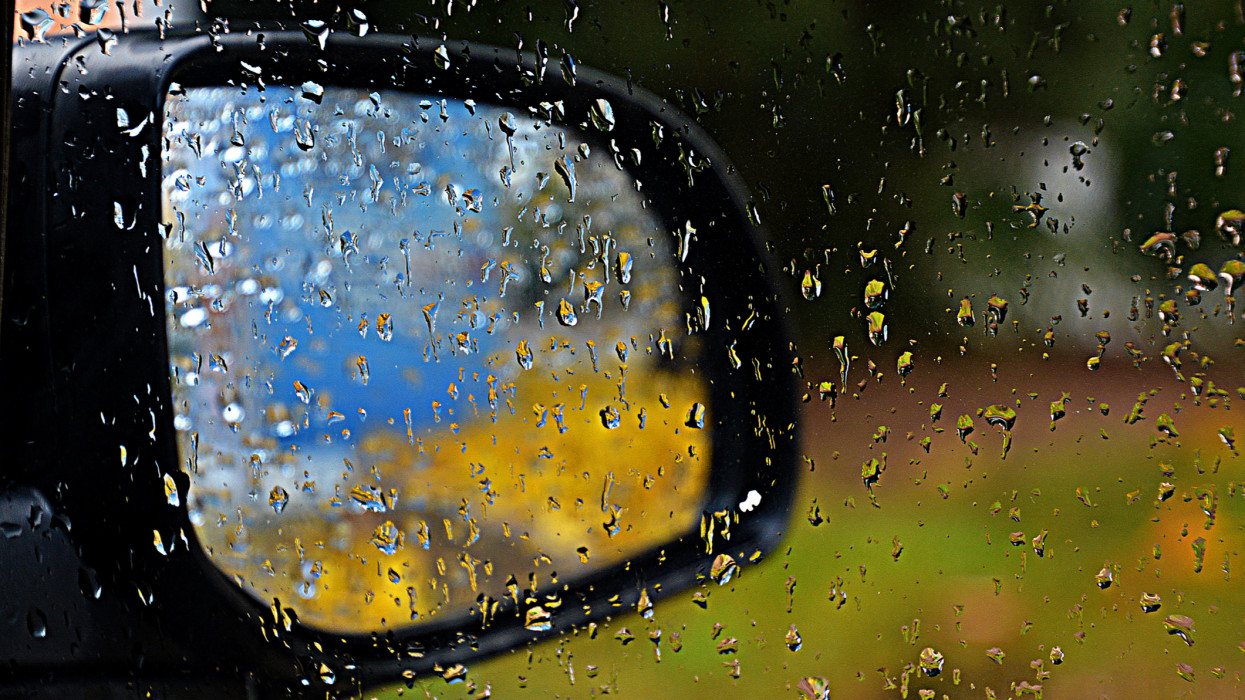 View  through the window of my car on the outside rear view mirror in which you can see bright colors reflected. On the window there were big raindrops. The rain was heavy and it was in December in South East of France , i was inside the car cimlapi