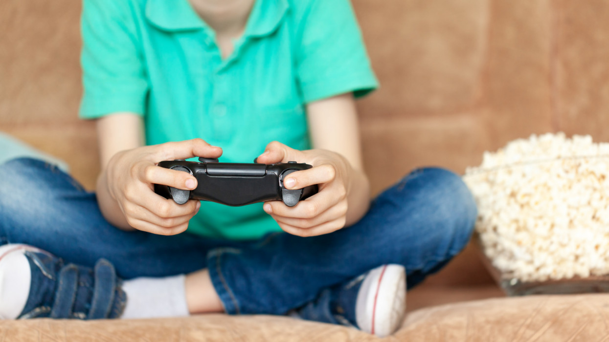 Child playing online video games and eating popcorn sitting on sofa in living room at home. Gaming video games concept. Closeup hands