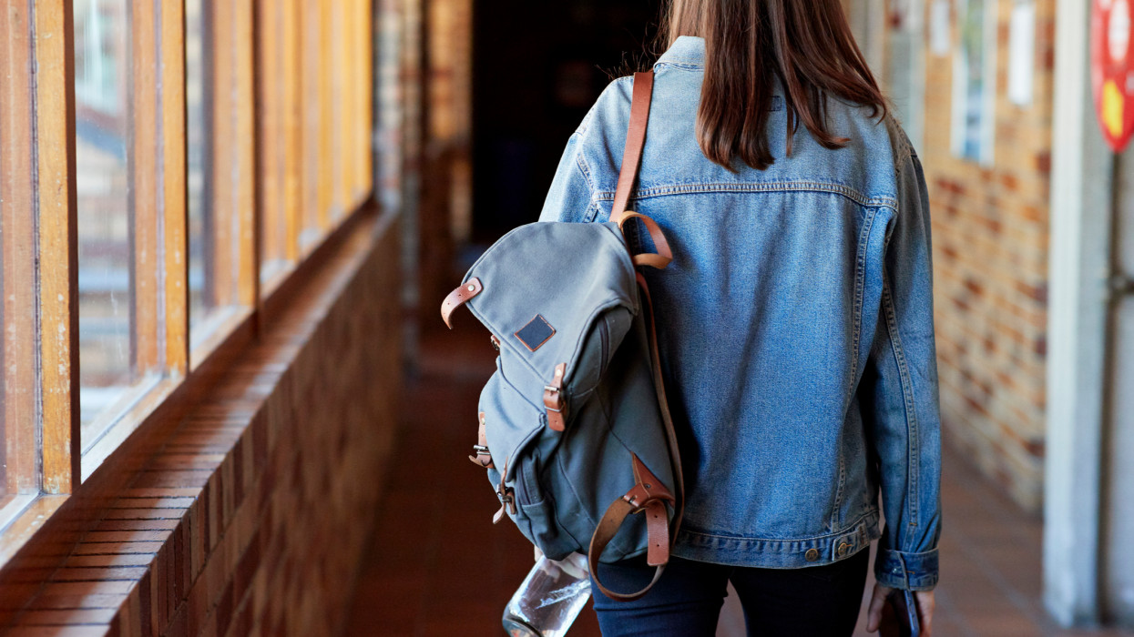 Rear view of young woman with backpack walking in corridor at university cimlapi