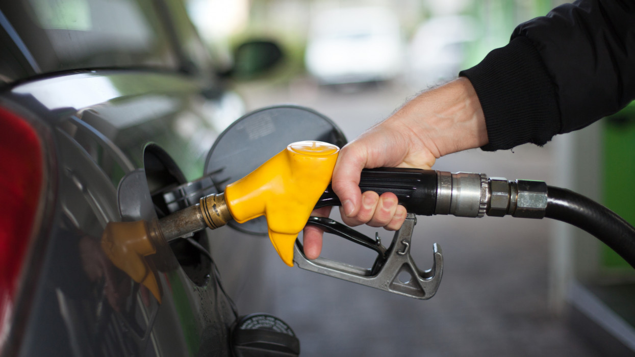 Hand of man fueling up a vehicle with a yellow gas pump.
