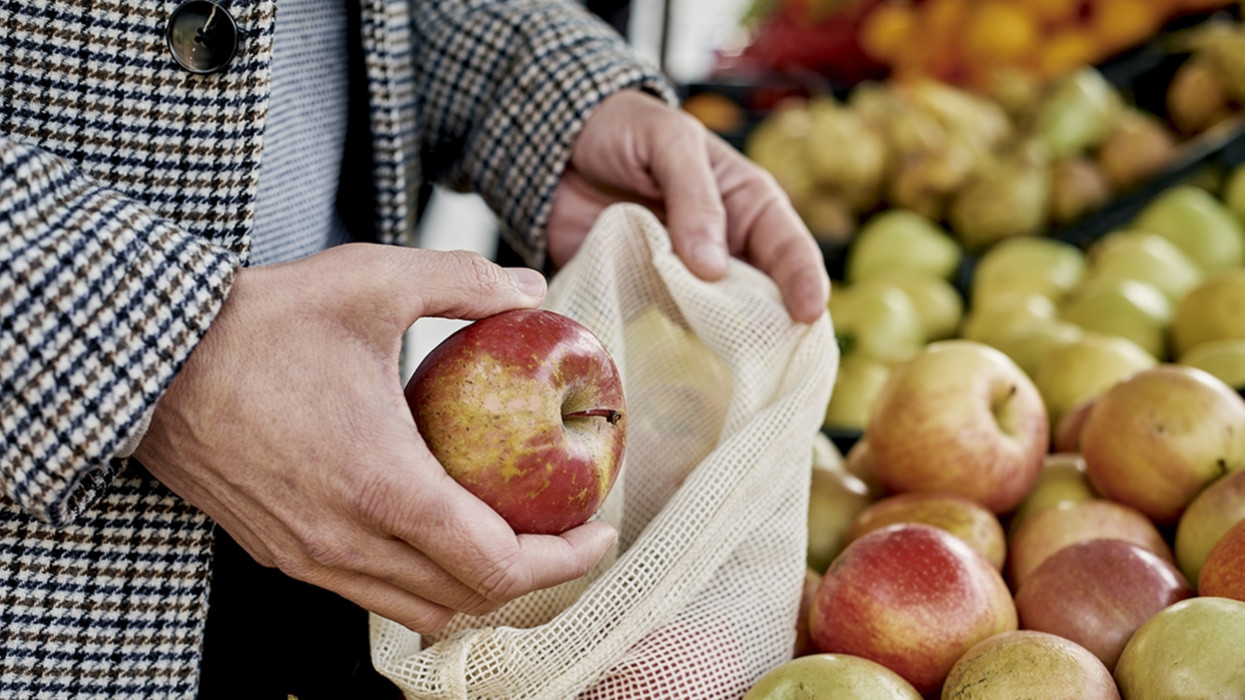 closeup of a man shopping at a greengrocer putting some red apples in a textile reusable mesh bag, as a measure to reduce plastic pollution