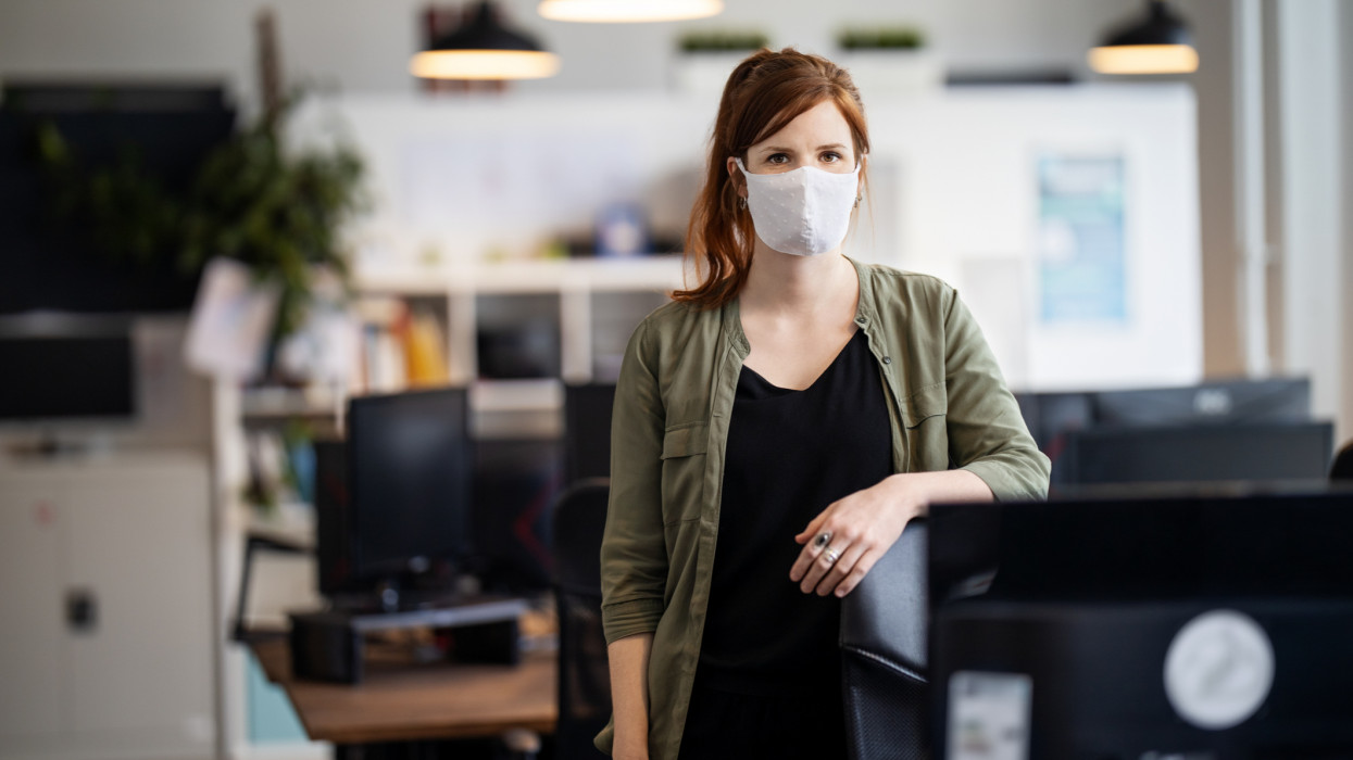 Portrait of a businesswoman back to work at office after pandemic lockdown. Female entrepreneur with protective face mask standing alone in office.