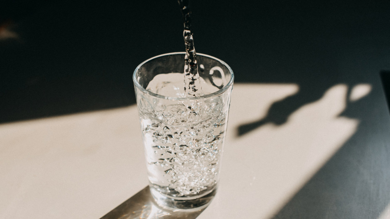 Water being poured in a glass of water that cast a beautiful shadow on a white kitchen countertop. Copy space.