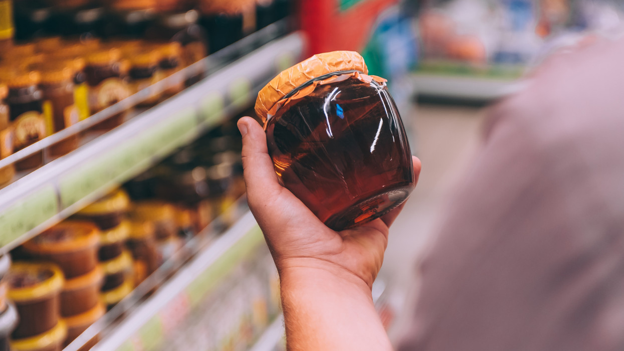 The guy in the supermarket holds a glass jar of honey
