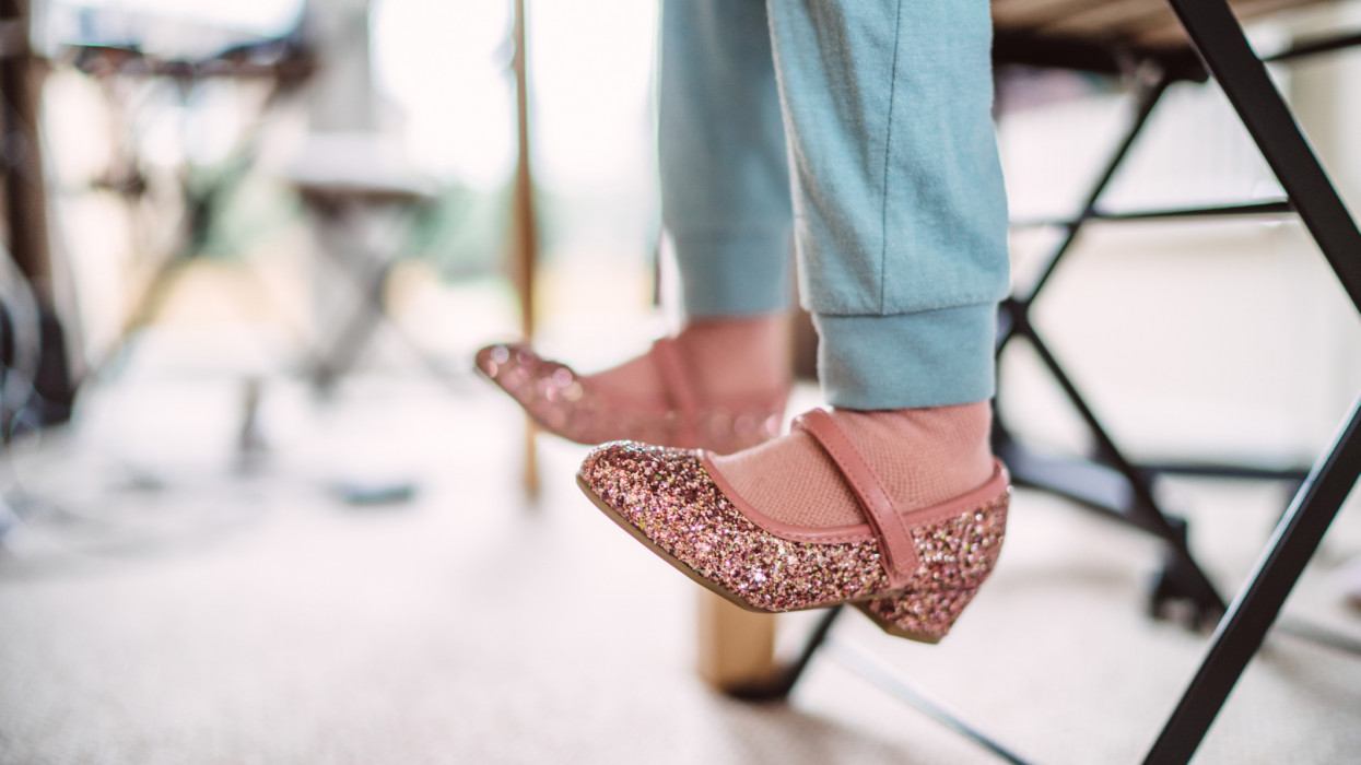 Close-up of little girlâs legs in a pair of glittery shoes & pyjamas under the table at home.