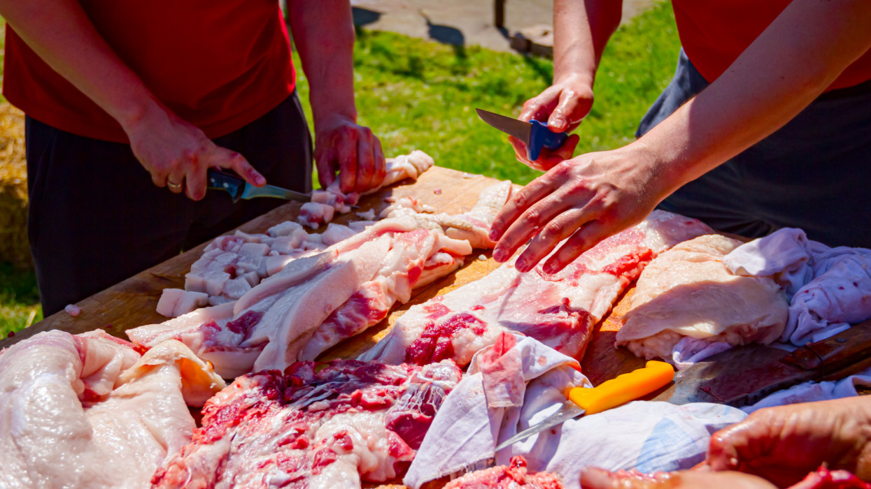 Butcher is cutting the raw pork meat into smaller pieces slice using sharp knife, prepares flesh for cooking.