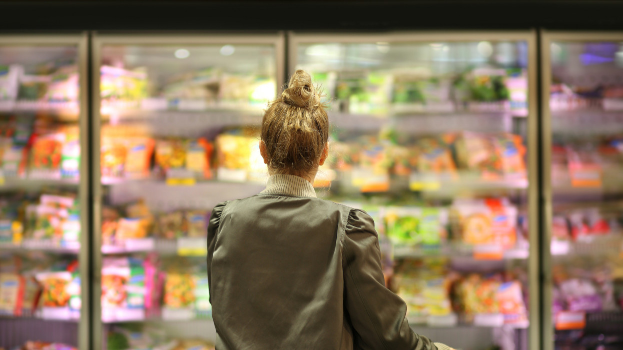 Woman choosing frozen food from a supermarket freezer. grocery store