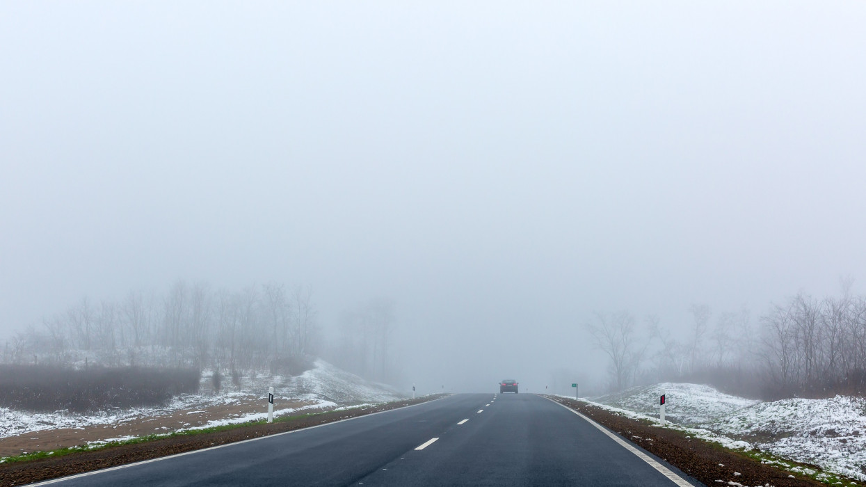 Traffic conditions on foggy morning on winter road. The car can barely be seen. Space for text. Selective focus