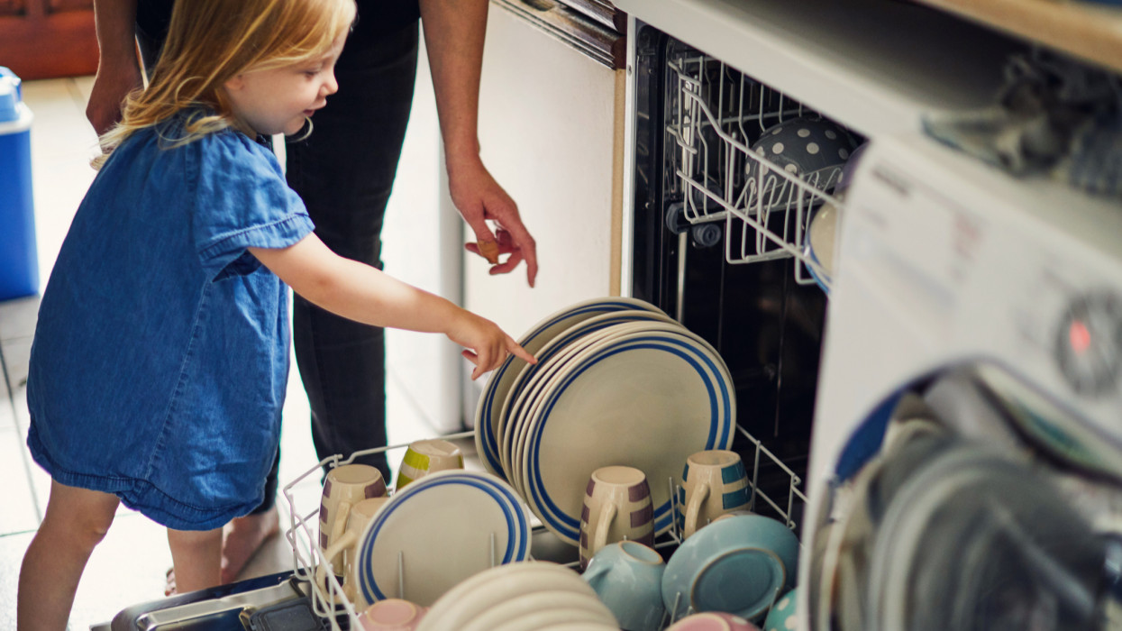 Young toddler girl helping to load the dishwasher