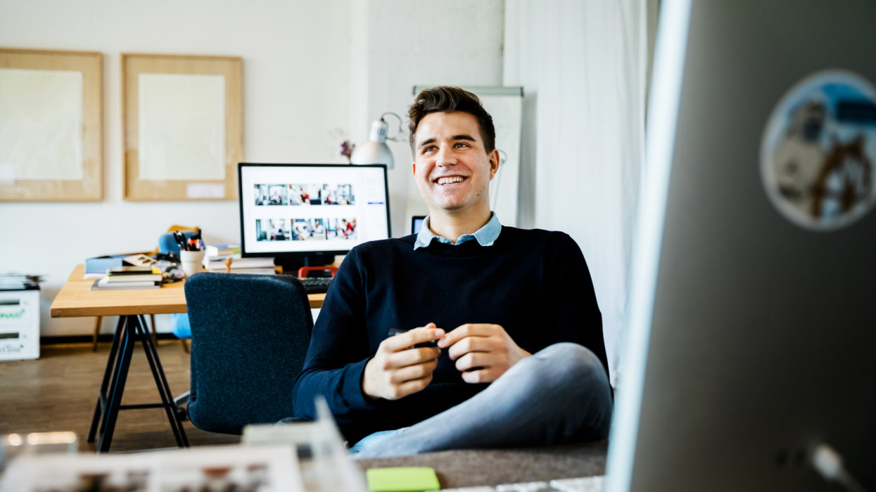 Portrait of young casual businessman sitting on his desk