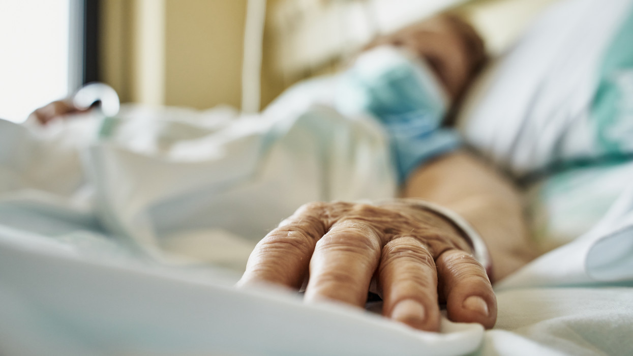 Senior woman wearing mask infected by coronavirus on hospital bed receiving medicine by drip. Close-up fingers of the senior patient Â´s hand while she is sleeping. Horizontal photo