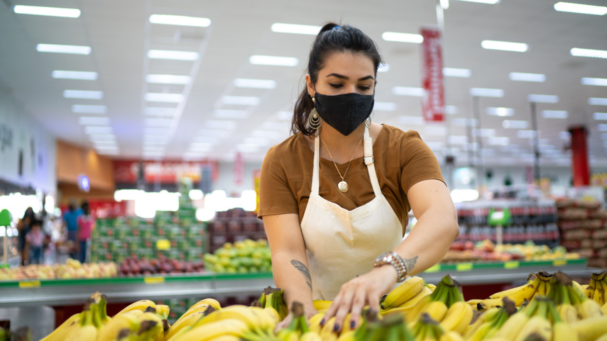 Young woman wearing face mask working in a supermarket arranging fruits