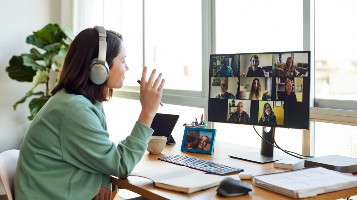 Female entrepreneur discussing with colleagues on video call. Businesswoman is sitting at table in home office. She is wearing headphones.