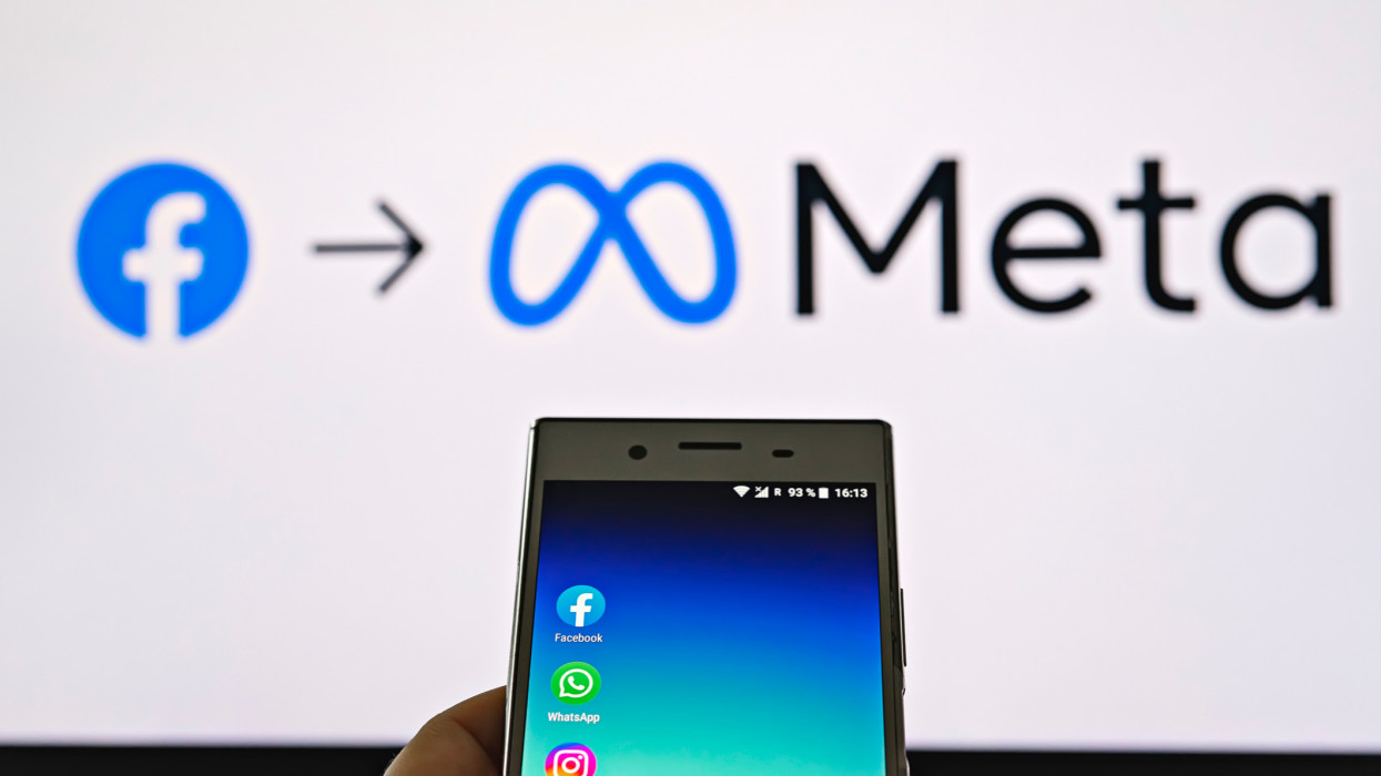 Smartphone display with logo of Facebook, WhatsApp and Instagram apps in hand against blurred META logotype on white monitor background: Tallinn, Estonia - October 29, 2021