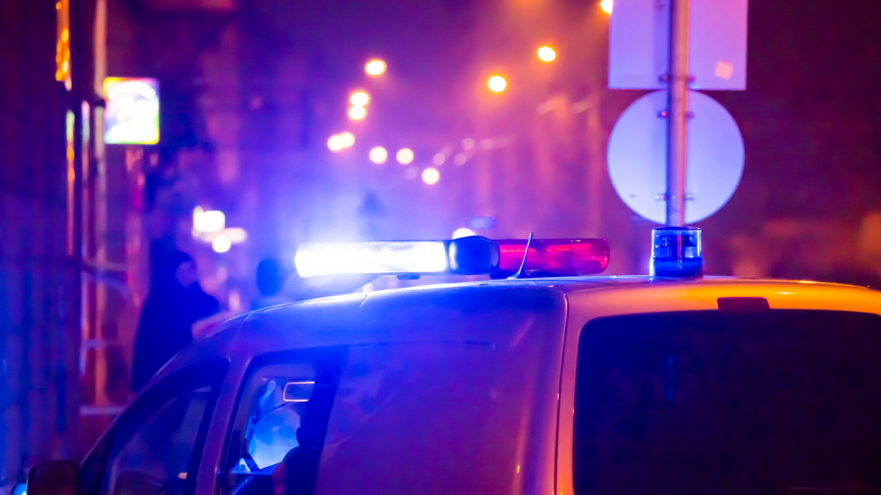 Police car in action with blinking light and siren signal at night in the city. Blurred bokeh background, public lighting lamps.